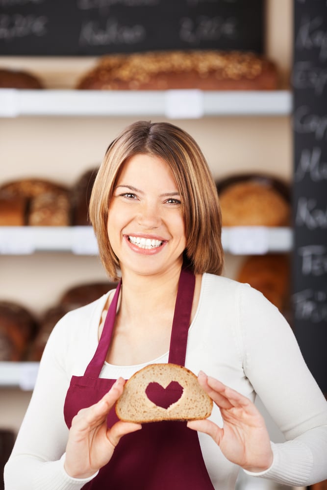 Close up portrait of cheerful woman holding bread with heart