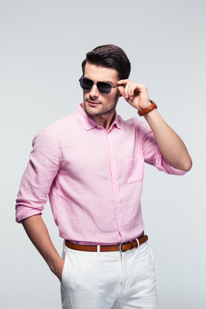 Portrait of a trendy young man in sunglasses and pink shirt over gray background