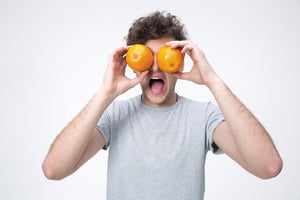 Surprised man looking through oranges over gray background